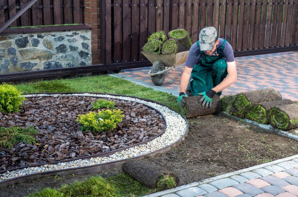 Ein Mann verlegt Rasenrollen für einen neuen Gartenrasen.